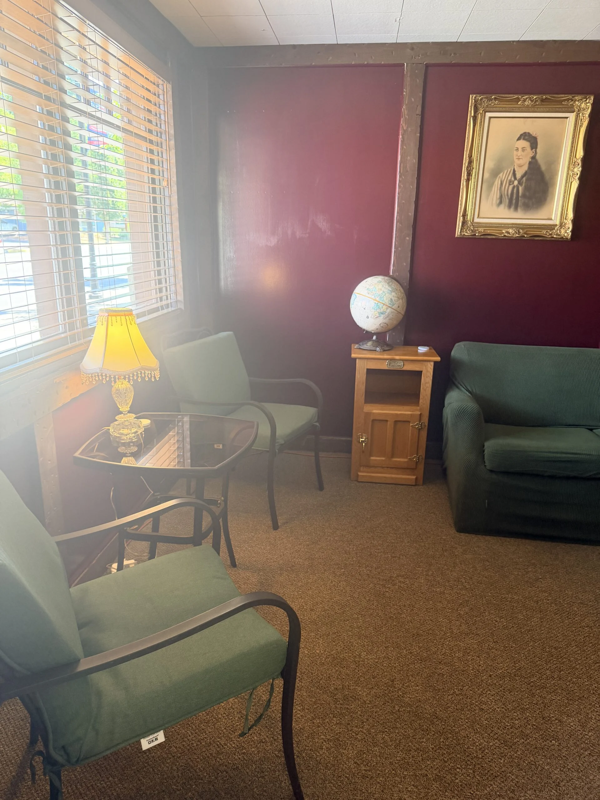 Reading nook with green armchairs, globe, lamp and framed portrait